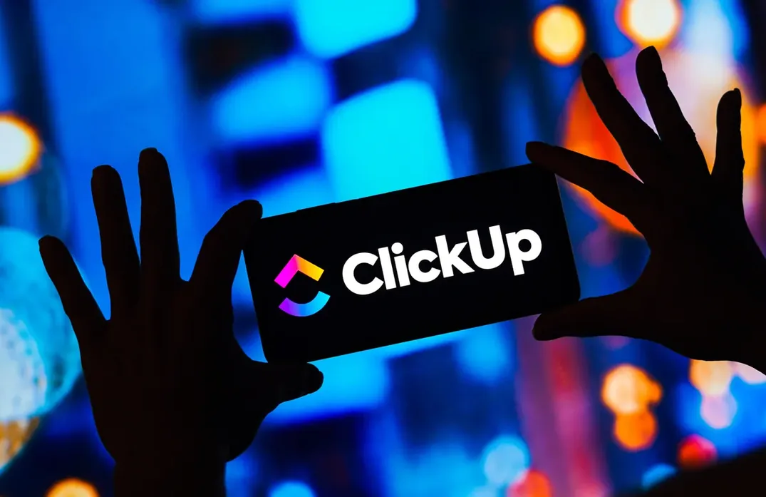Marca ClickUp em painel retroiluminado, com mãos escurecidas na frente